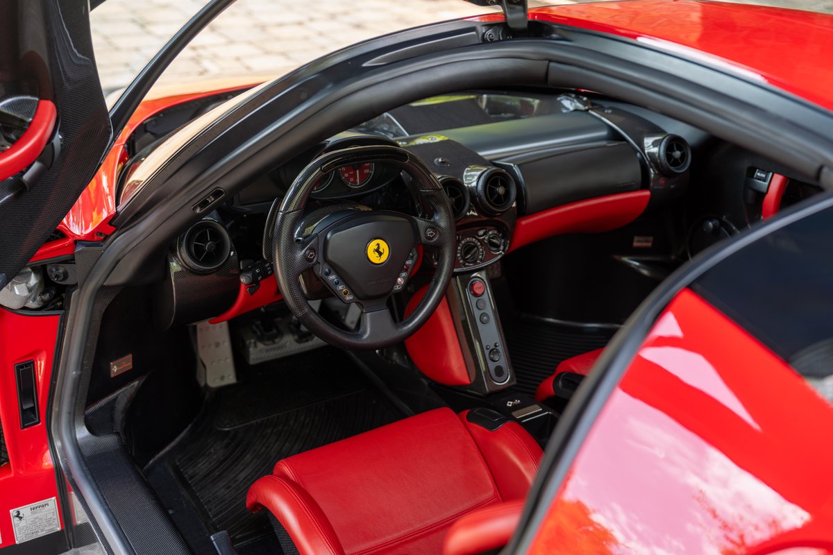 Interior of a red 2003 Ferrari Enzo, featuring red leather seats, carbon fiber trim, and a Formula 1-inspired steering wheel.
