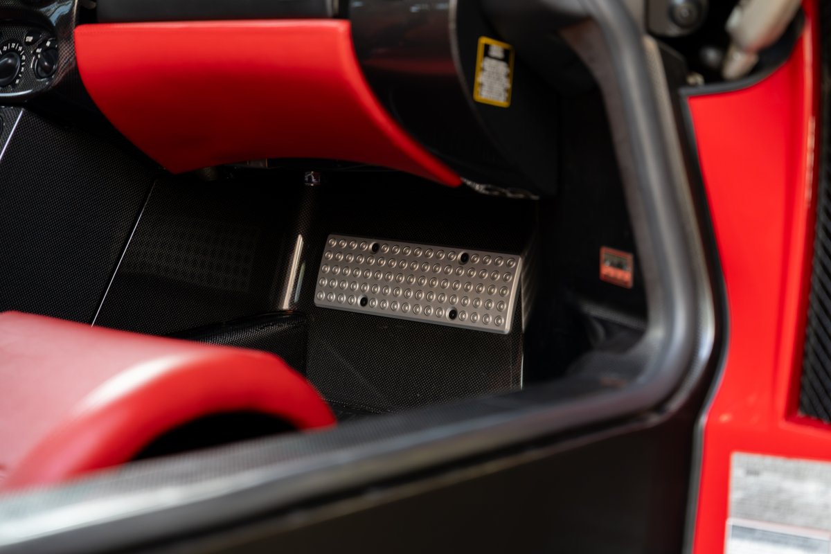 Close-up of brushed metal foot pedals and red interior trim in a 2003 Ferrari Enzo.