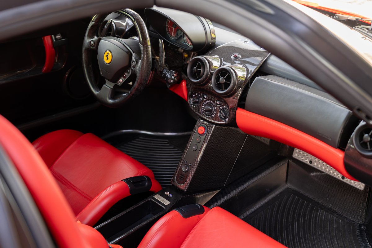 Interior view of a red 2003 Ferrari Enzo, featuring red leather seats and carbon fiber trim.
