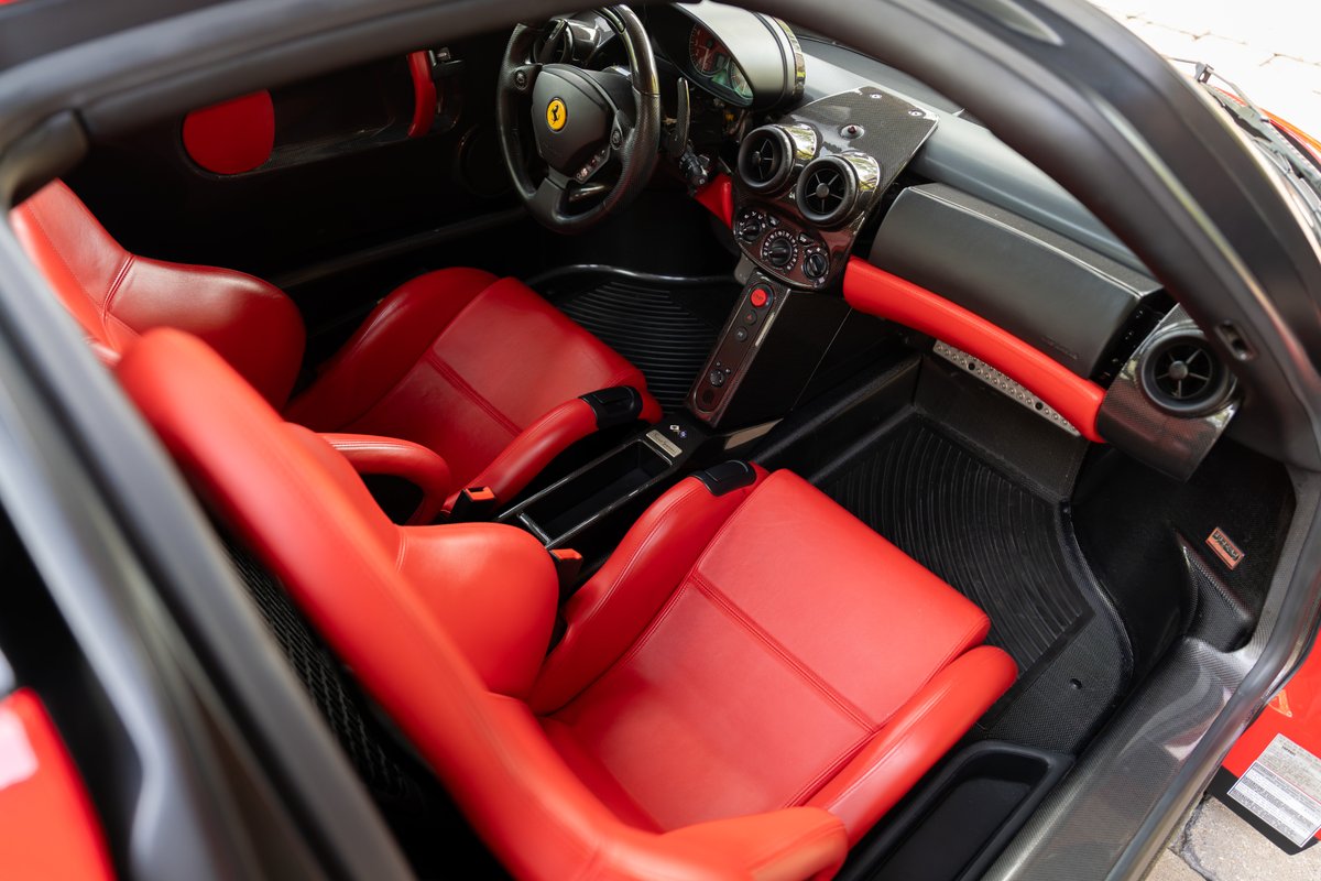 Ferrari Enzo interior with red leather seats, carbon fiber trim, and black floor mats.