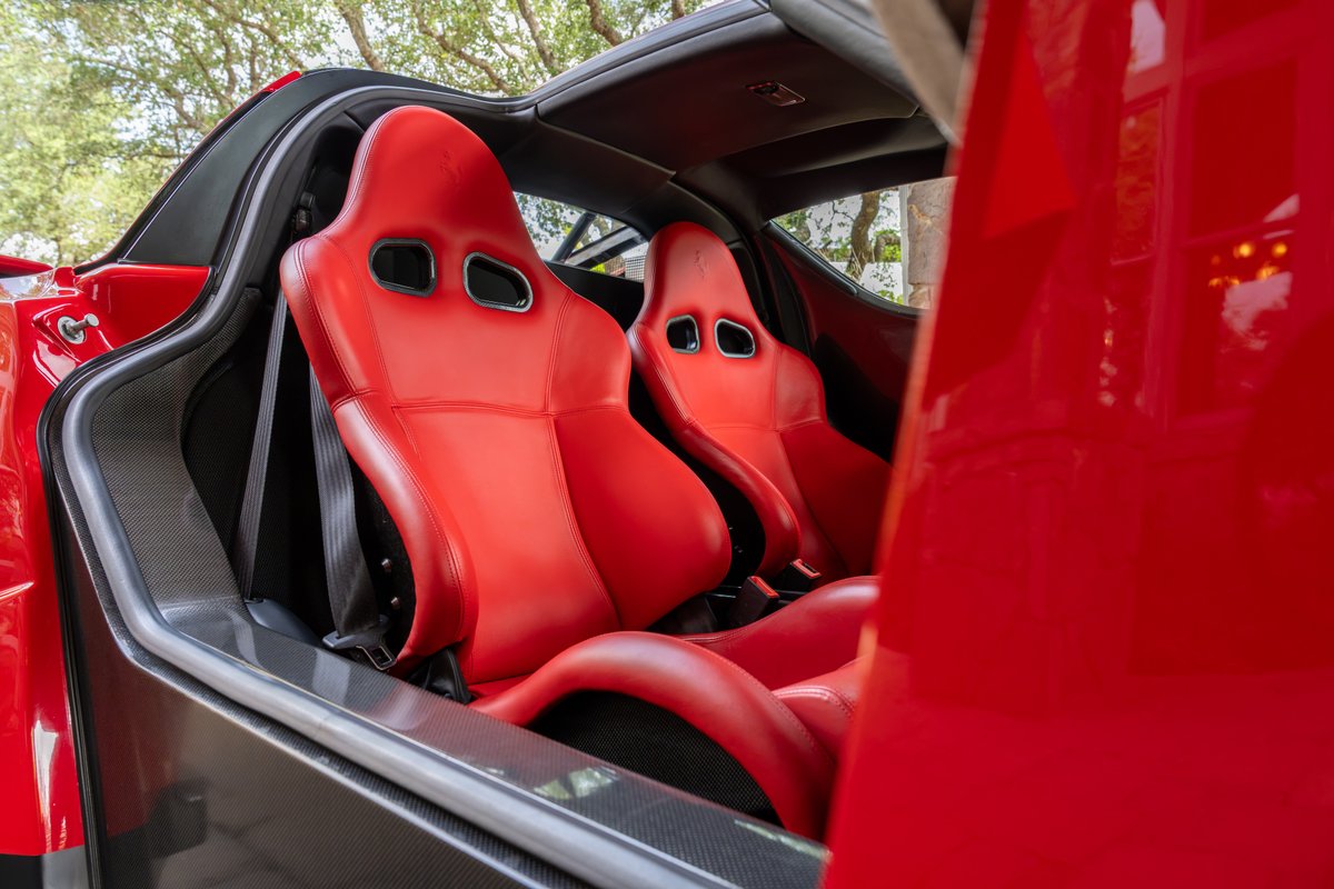 Interior of a red 2003 Ferrari Enzo showing two red leather racing seats and carbon fiber trim.