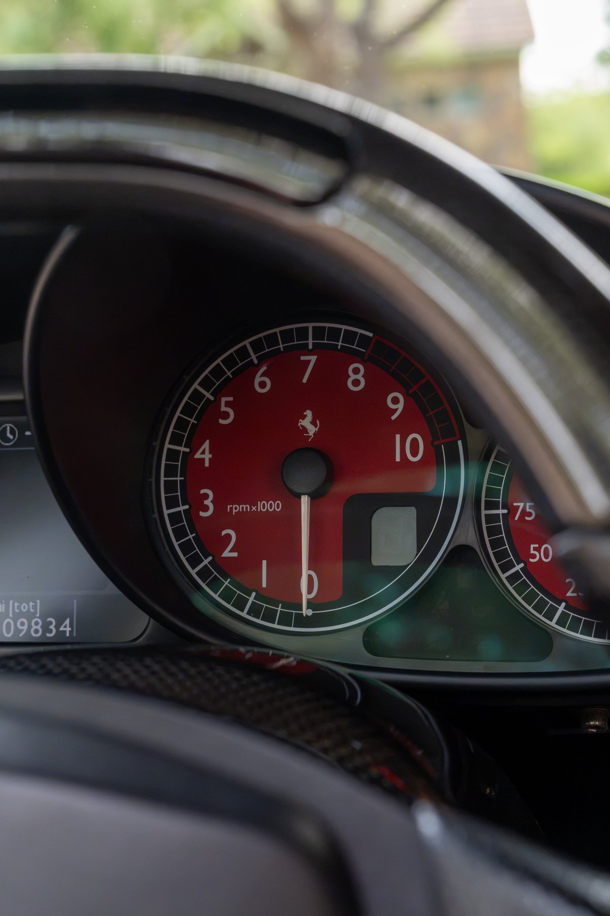 Red Ferrari Enzo tachometer and dashboard with carbon fiber trim and racing steering wheel.