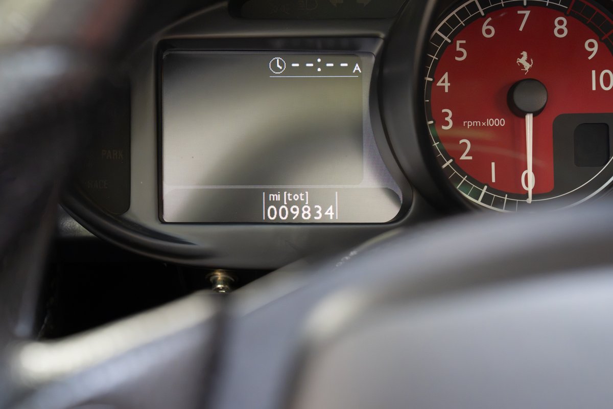 Ferrari Enzo dashboard: odometer shows 9834 miles. Red tachometer with Ferrari logo.
