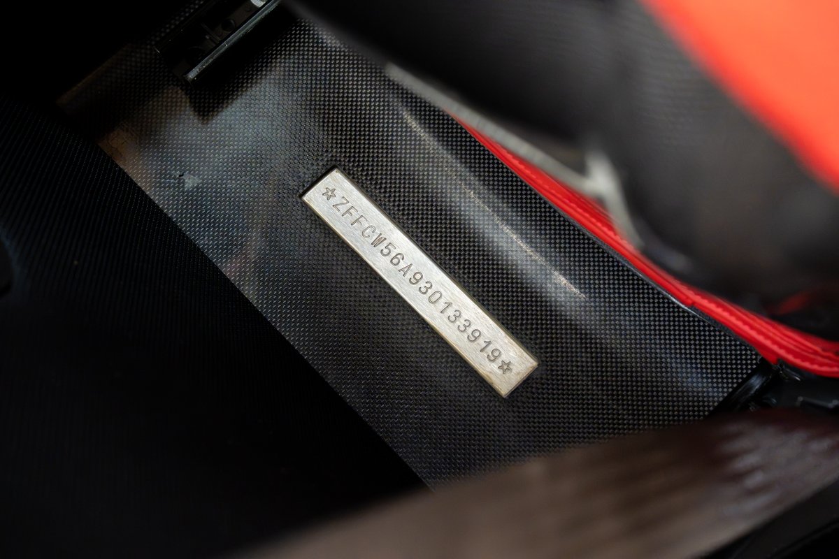 Ferrari Enzo VIN plate, with part of the carbon fiber trim and red interior visible.