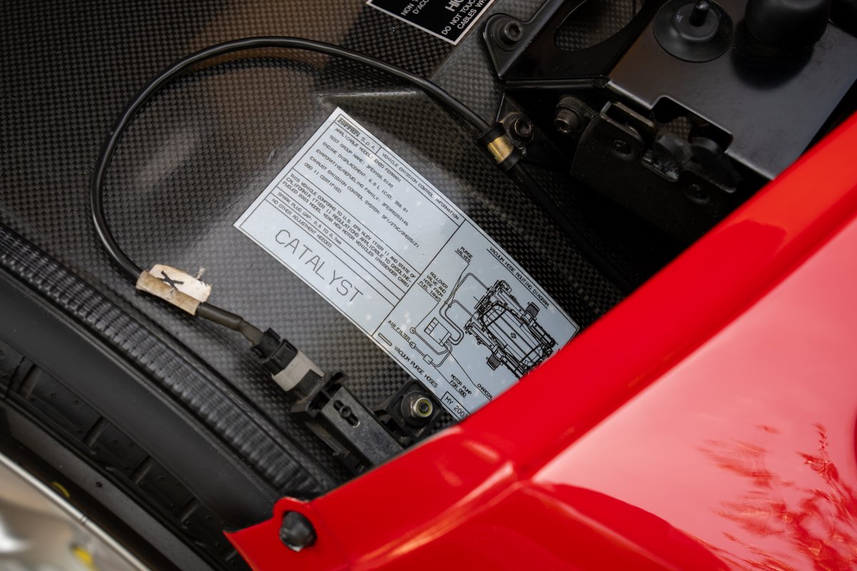 Closeup of a red 2003 Ferrari Enzo's carbon fiber engine bay with a catalyst label.