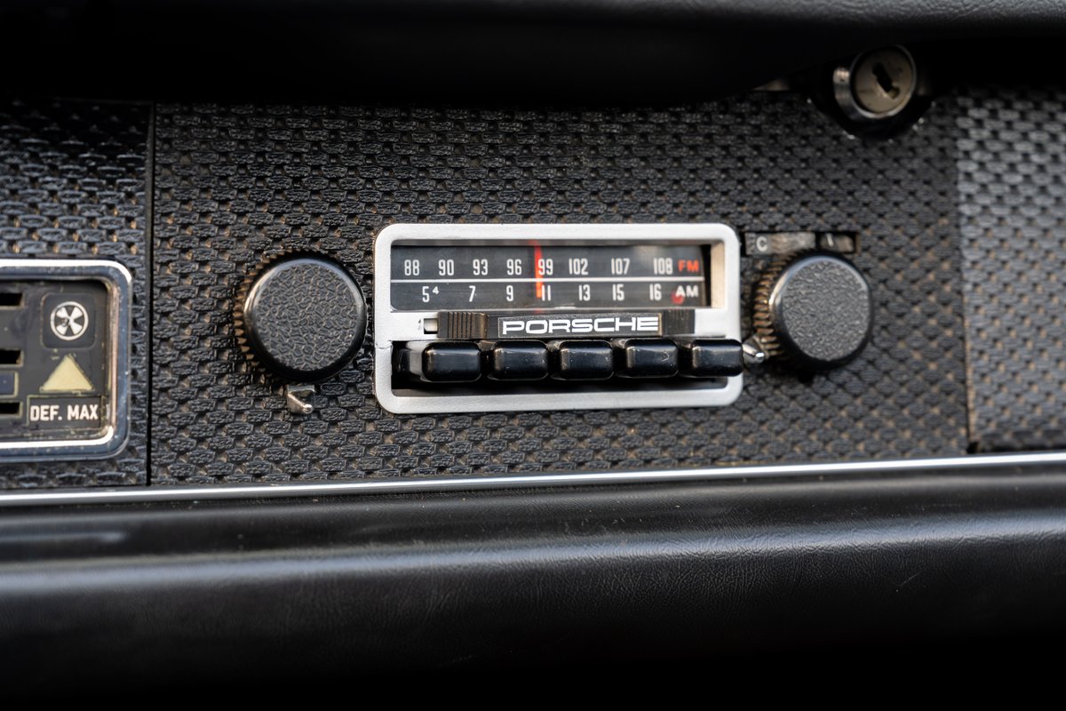 Close-up of a vintage Porsche 914 dashboard radio with AM/FM tuner and push buttons.