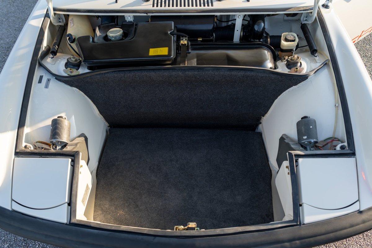 Front trunk of a white 1974 Porsche 914 Can-Am LE, showing carpeted storage and spare tire well.