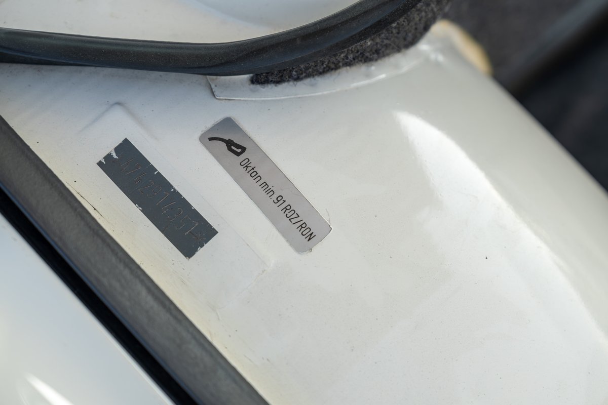Close-up of white 1974 Porsche 914 fuel door sticker indicating minimum 91 octane fuel.