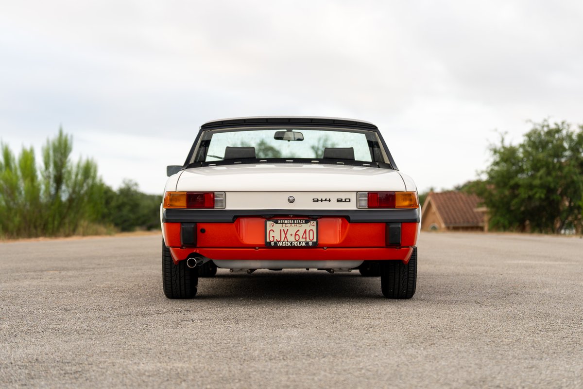 1974 Porsche 914 Can-Am in creamsicle orange and white, rear view. Features black trim and standard rims.