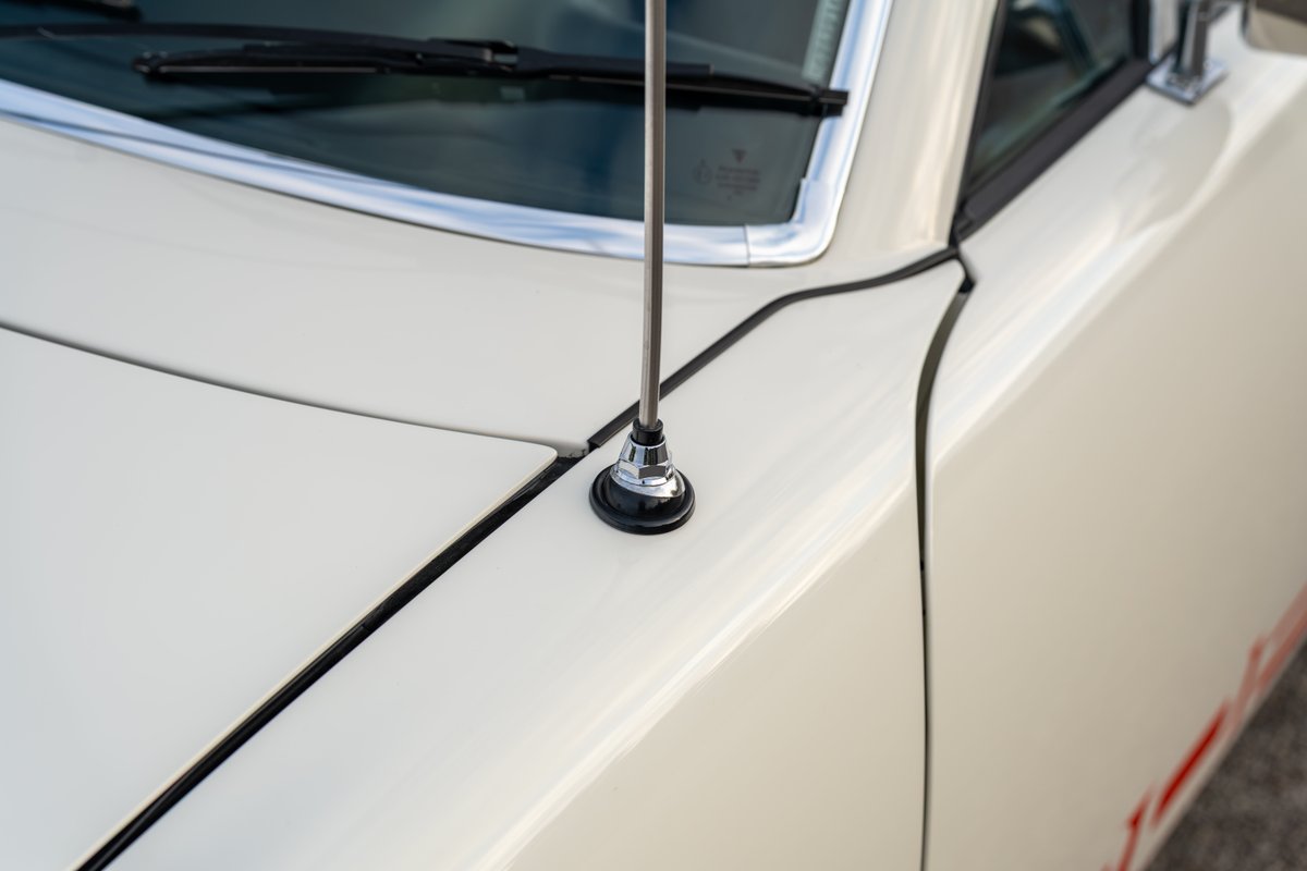 Close-up of a vintage white 1974 Porsche 914's fender with a chrome antenna base.