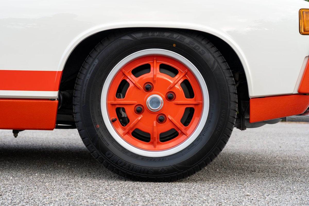 Close-up of an orange Fuchs rim and tire on a white 1974 Porsche 914 with orange racing stripes.