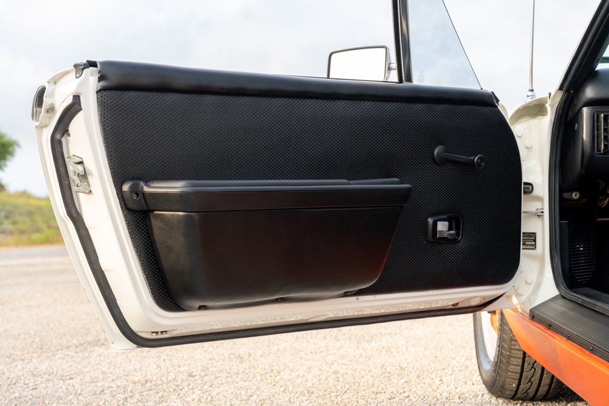1974 Porsche 914 interior door panel, featuring textured black trim, a black armrest, and a manual window crank.