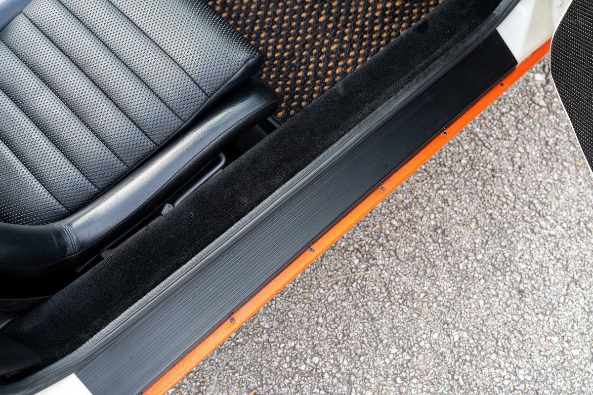 1974 Porsche 914 interior: perforated black leather seat, orange door trim, black carpet.