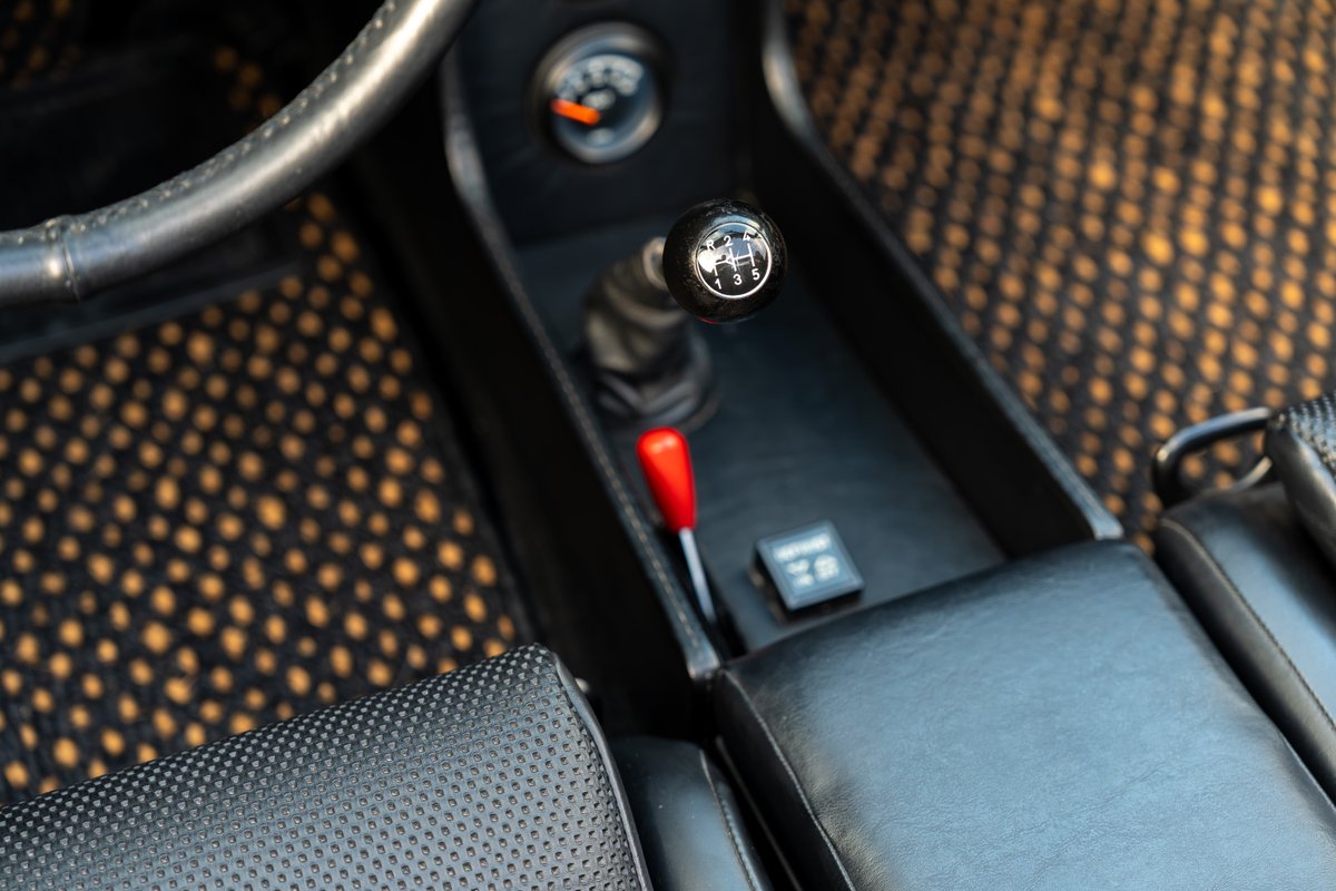Close-up of a 1974 Porsche 914 Can-Am interior with a 5-speed manual shifter and patterned floor mats.