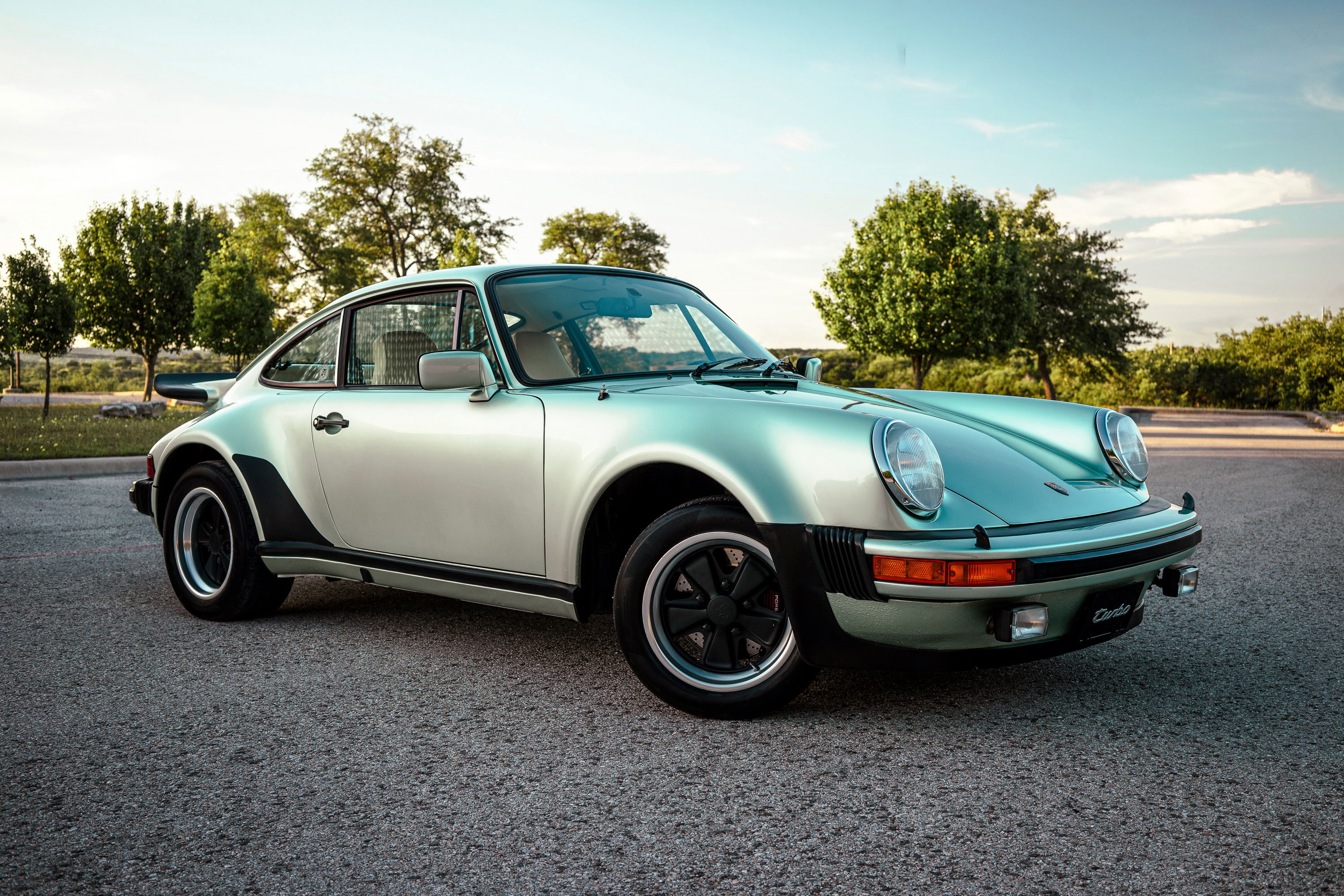 Stunning Ice Metallic Green 1976 Porsche 930 Turbo, showcasing its widebody, iconic whale tail, and black Fuchs alloy wheels.