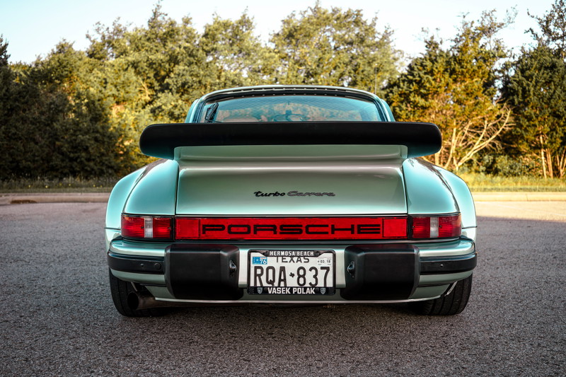 1976 Ice Metallic Green Porsche 930 Turbo rear, iconic whale tail wing, PORSCHE taillight bar, 'turbo Carrera' script, black bumperettes.
