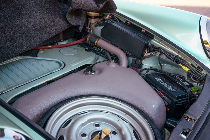 Vintage 1976 Porsche 930 frunk in Ice Metallic Green, showing steel spare wheel, fuel tank, and Prostart battery.