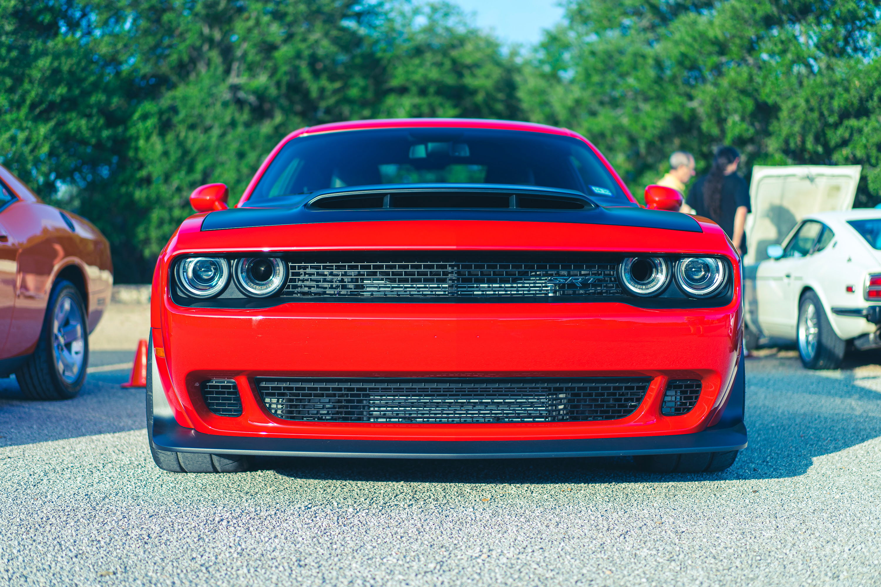 Red Dodge Challenger SRT muscle car with black hood scoop, aggressive front fascia, and twin projector headlights at a car meet.