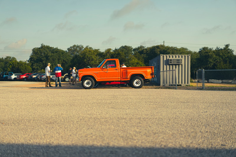 Vibrant orange 1978 Ford F-150 Ranger XLT Dentside pickup at a car meet, featuring white steel rims & chrome trim.