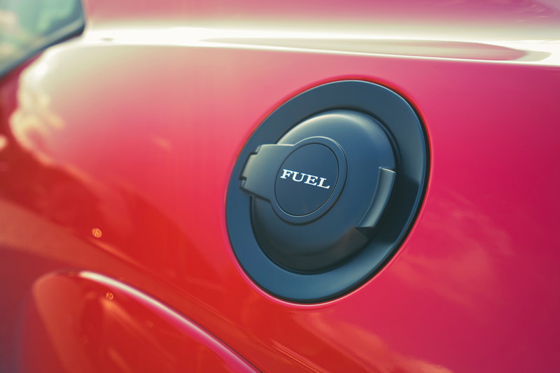 Close-up of a vibrant red Dodge Challenger's matte black fuel filler cap, featuring "FUEL" embossed lettering.