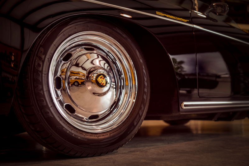 Gloss black Porsche 356 Speedster fender detail, showing gold "Speedster" badging, chrome side trim, and full-disc hubcap with Porsche crest.