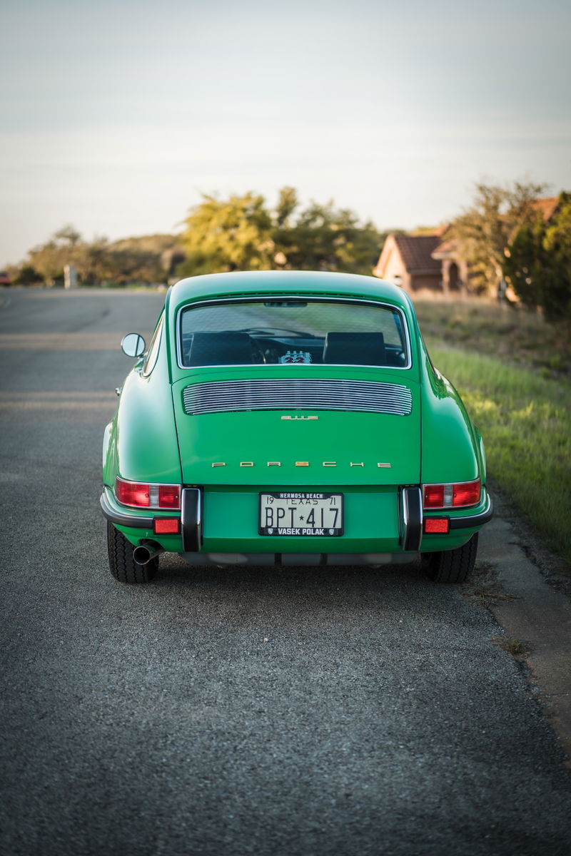 Rear of a Conda Green 1971 Porsche 911E. Features chrome "PORSCHE" script, slatted engine grille, bumperettes, and Texas plate.