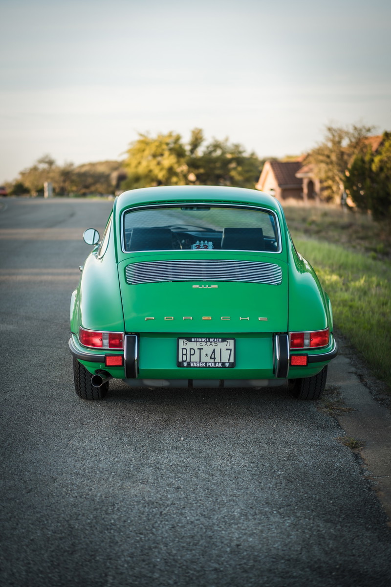 Rear of a Conda Green 1971 Porsche 911E. Features chrome "PORSCHE" script, slatted engine grille, bumperettes, and Texas plate.