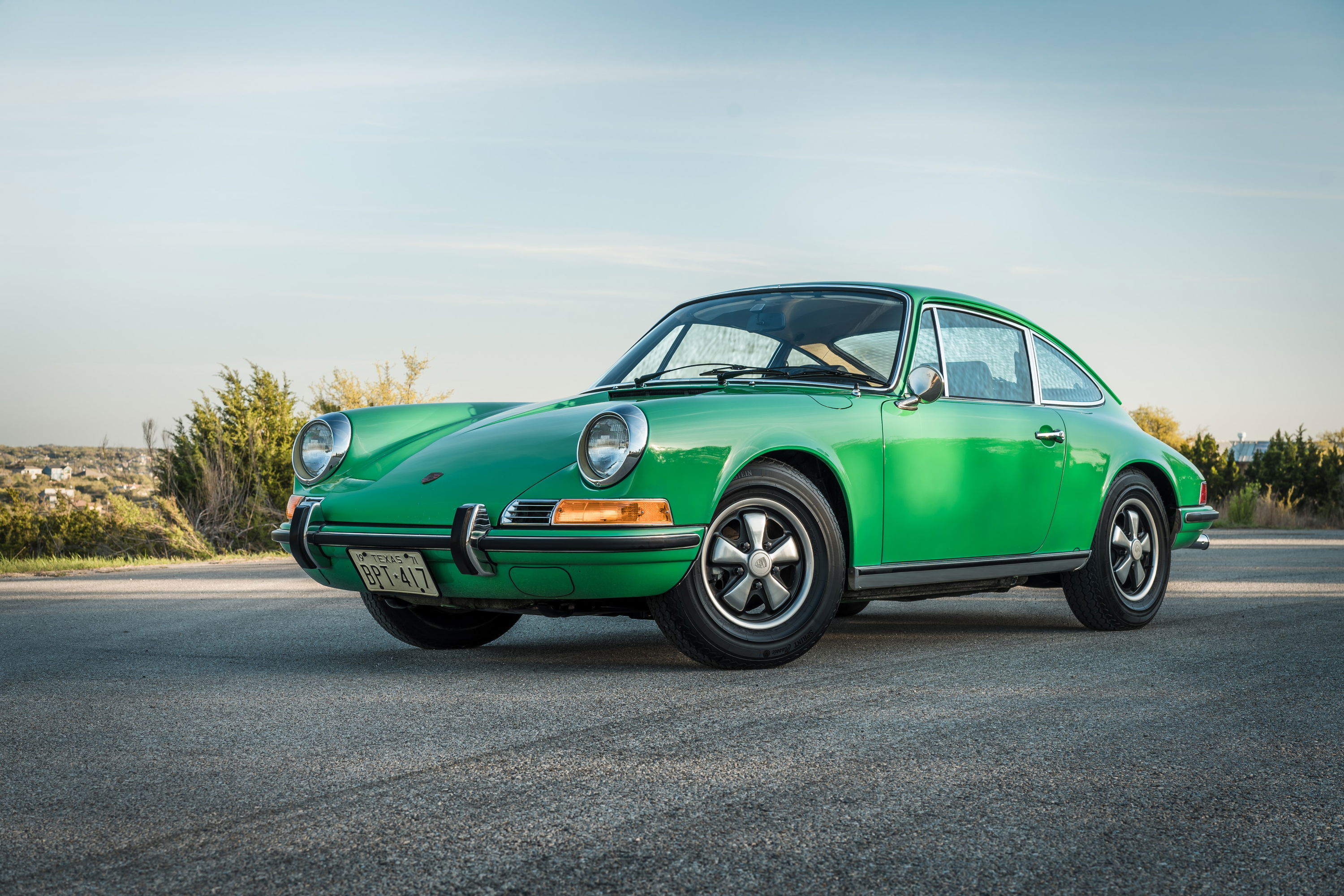 Front 3/4 view of a vibrant Conda Green 1971 Porsche 911E coupe with polished chrome trim and Fuchs wheels.