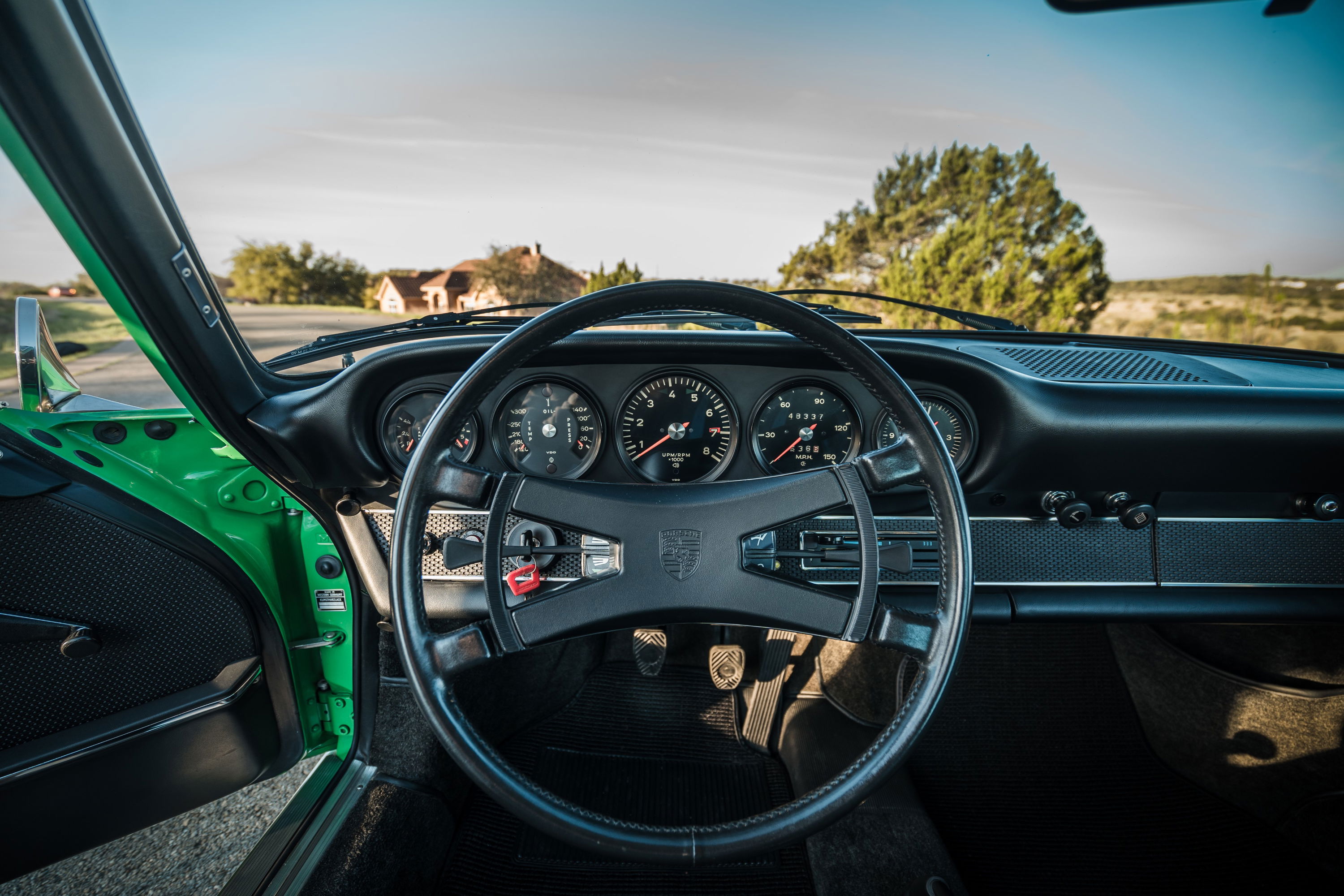 Conda Green 1971 Porsche 911E interior. Classic black dashboard, 5-dial instrument cluster, period steering wheel, and manual pedals.