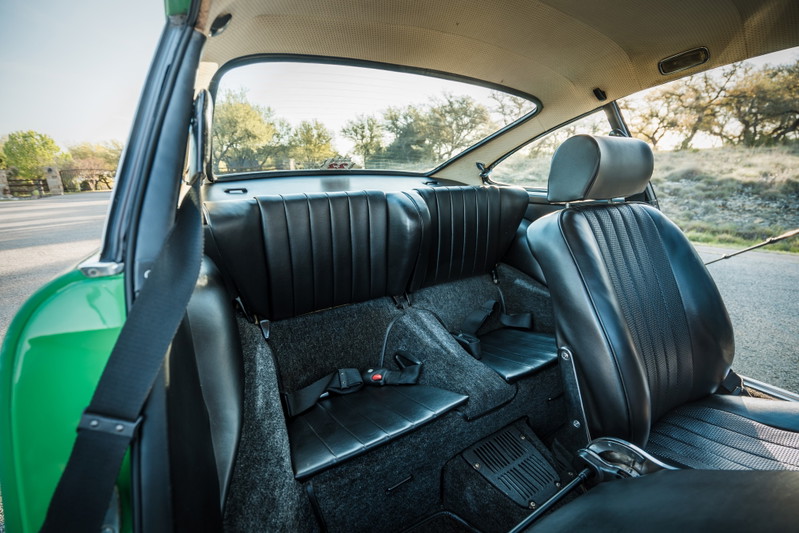 Interior view of a Conda Green 1971 Porsche 911E, featuring black leather seats, dark grey carpet, and a perforated headliner.