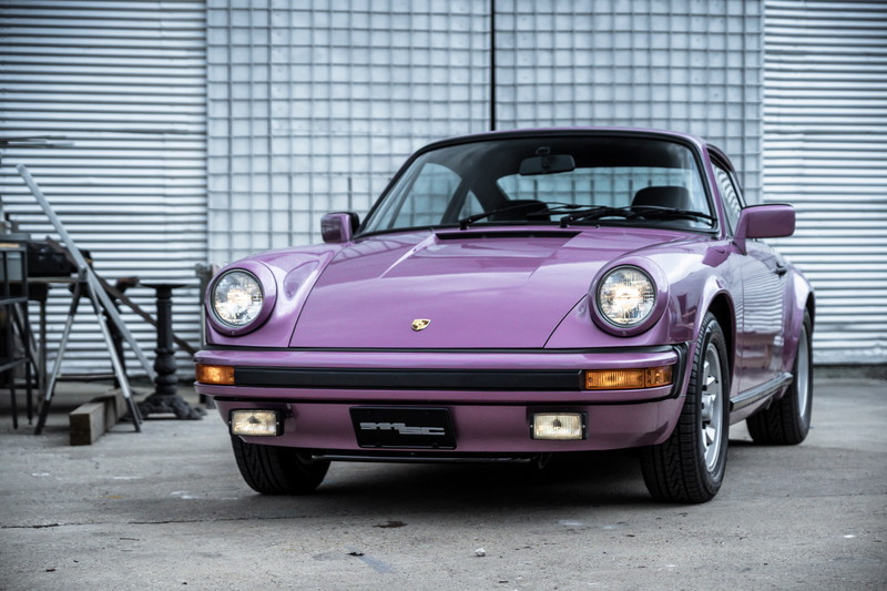 Vibrant purple Porsche 911SC, front view, showcasing its classic Fuchs rims, black bumper trim, and bright headlights.