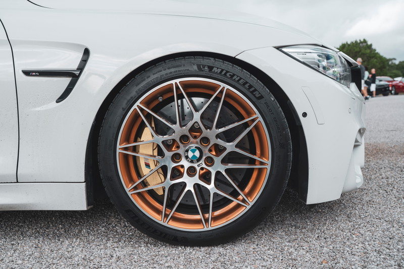 White BMW M4 coupe showcasing Frozen Gold multi-spoke M Performance wheels, Michelin PS4S tires, and large gold M brake calipers.