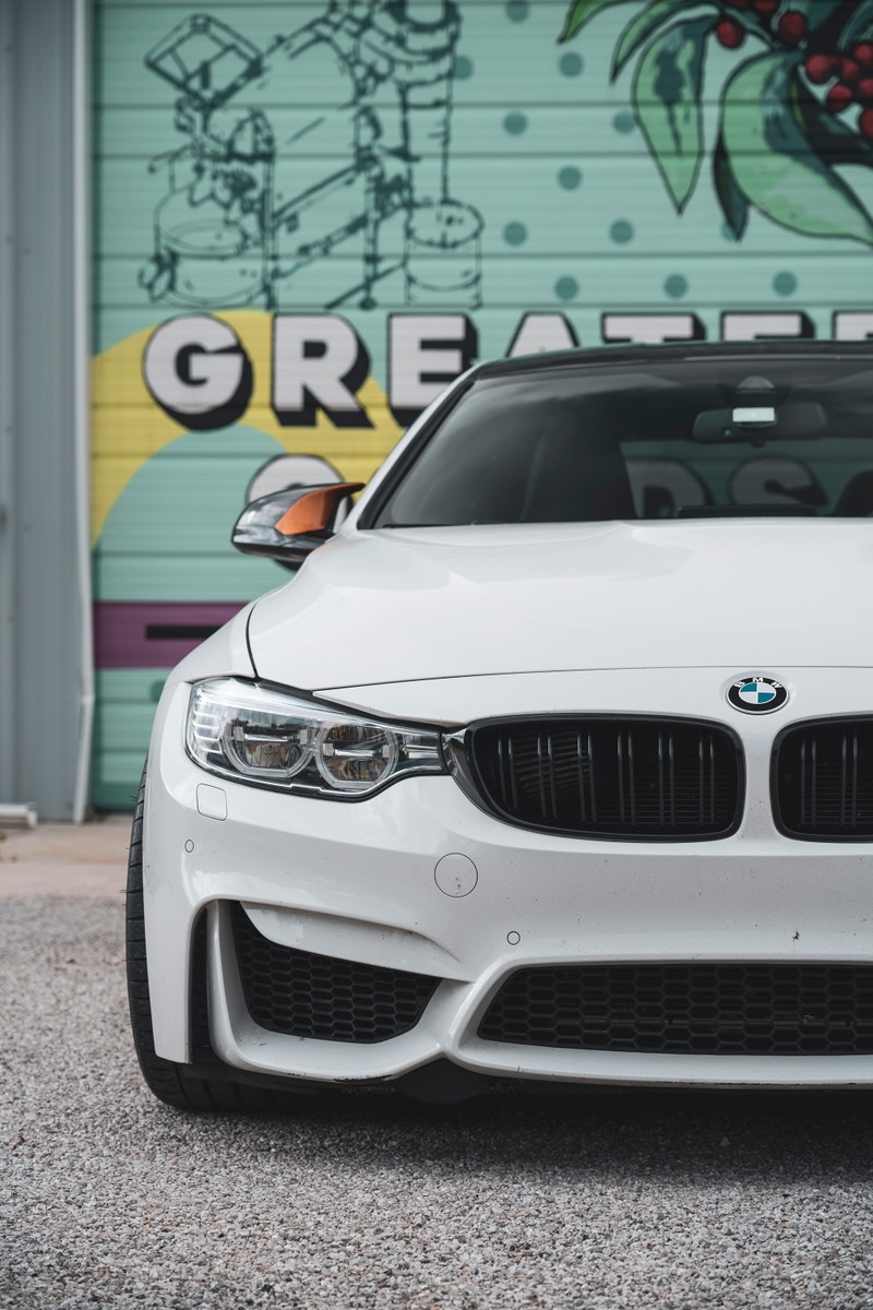Front end of an Alpine White BMW M4 coupe featuring black M-kidney grilles, LED headlights, & M-sport aero.