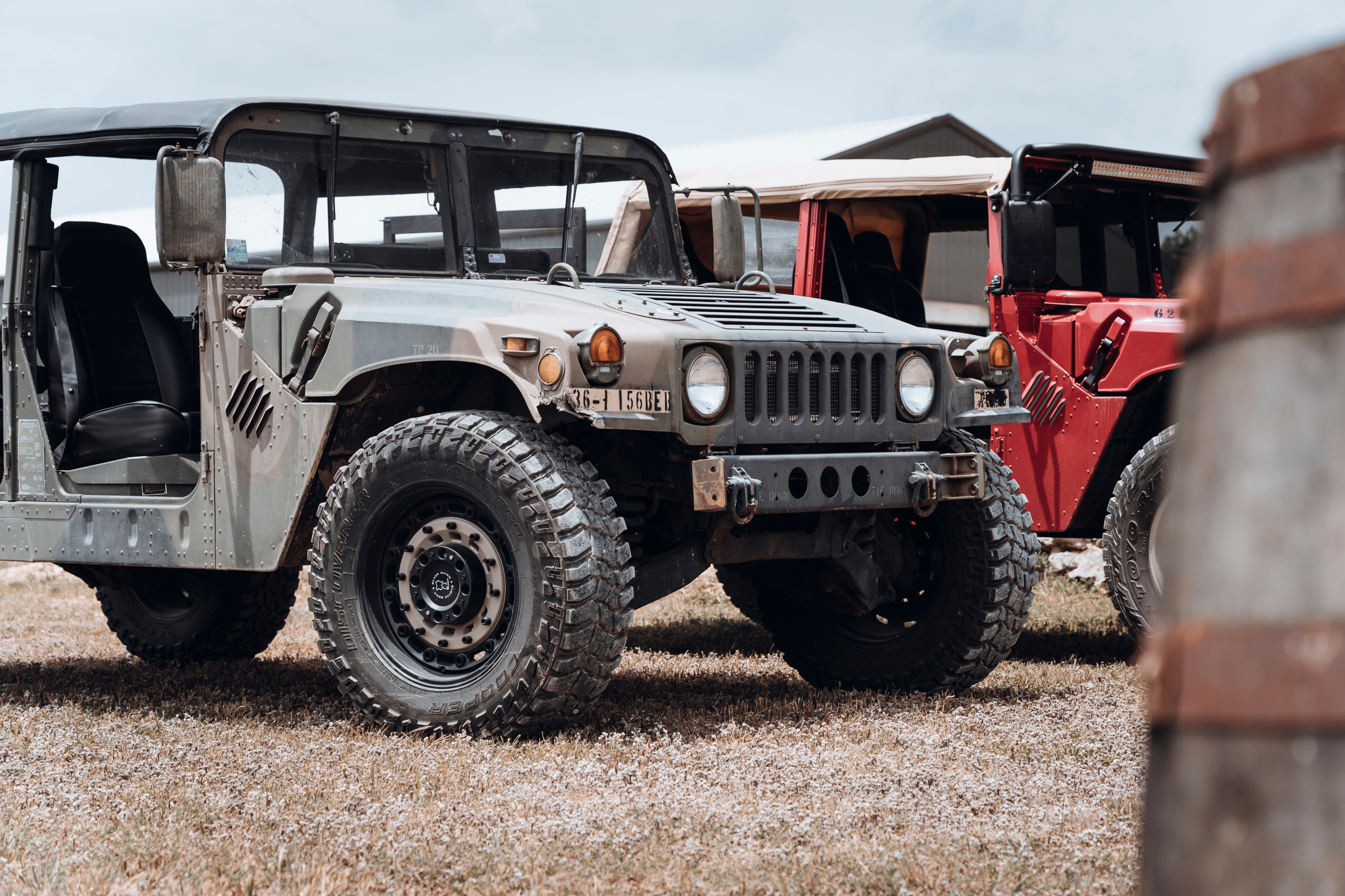 Olive drab HMMWV showcases Black Rhino beadlock rims, Cooper Discoverer STT Pro tires, and heavy-duty bumper at a car show.