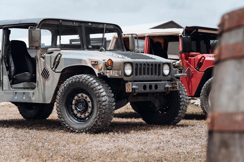 Olive drab HMMWV showcases Black Rhino beadlock rims, Cooper Discoverer STT Pro tires, and heavy-duty bumper at a car show.