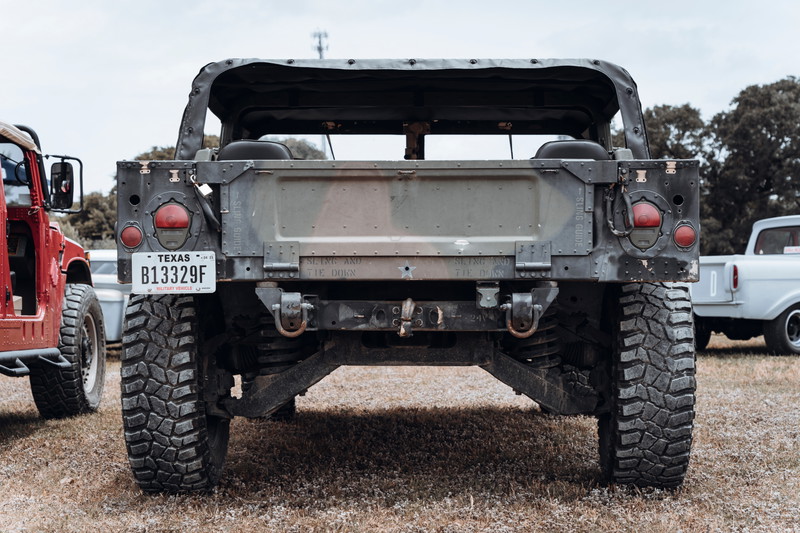 Rear of an olive drab military HMMWV (Humvee) with a soft top & rugged mud-terrain tires. Features heavy-duty recovery points.