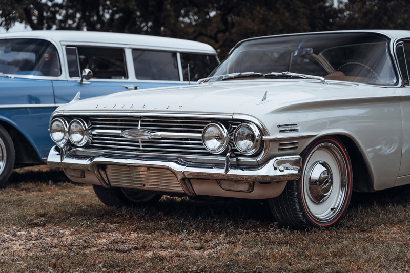 Front view of a classic light cream 1961 Chevrolet Impala sedan, featuring quad headlights, chrome grille, and redline tires on white rims.