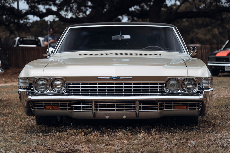 Gold 1967 Chevrolet Impala front view, featuring stacked quad headlights, prominent chrome grille, and black vinyl roof.