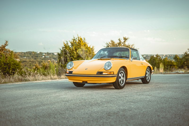 Front 3/4 view of a Signal Yellow 1973 Porsche 911S Targa with classic Fuchs rims, parked outdoors.