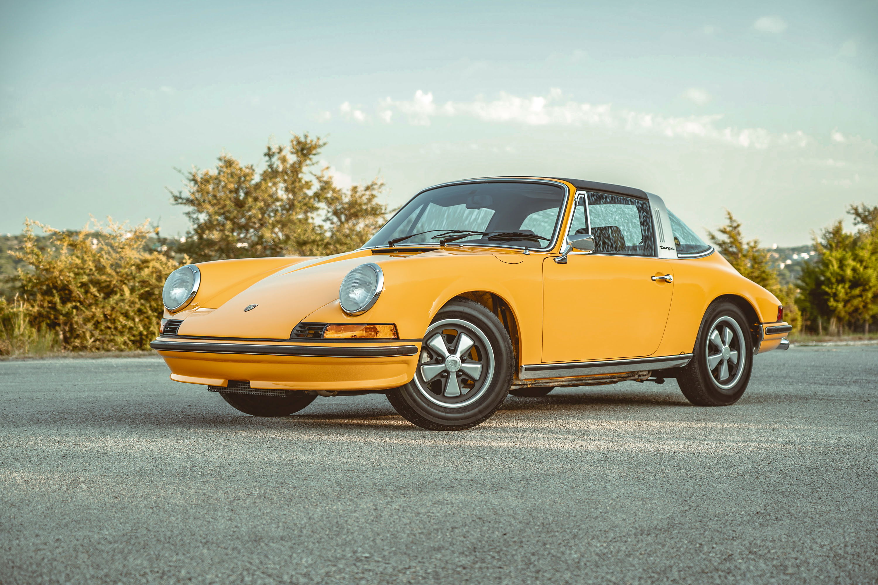 Signal Yellow 1973 Porsche 911S Targa. Features include black targa roof, classic Fuchs rims, chrome trim, and impact bumpers.