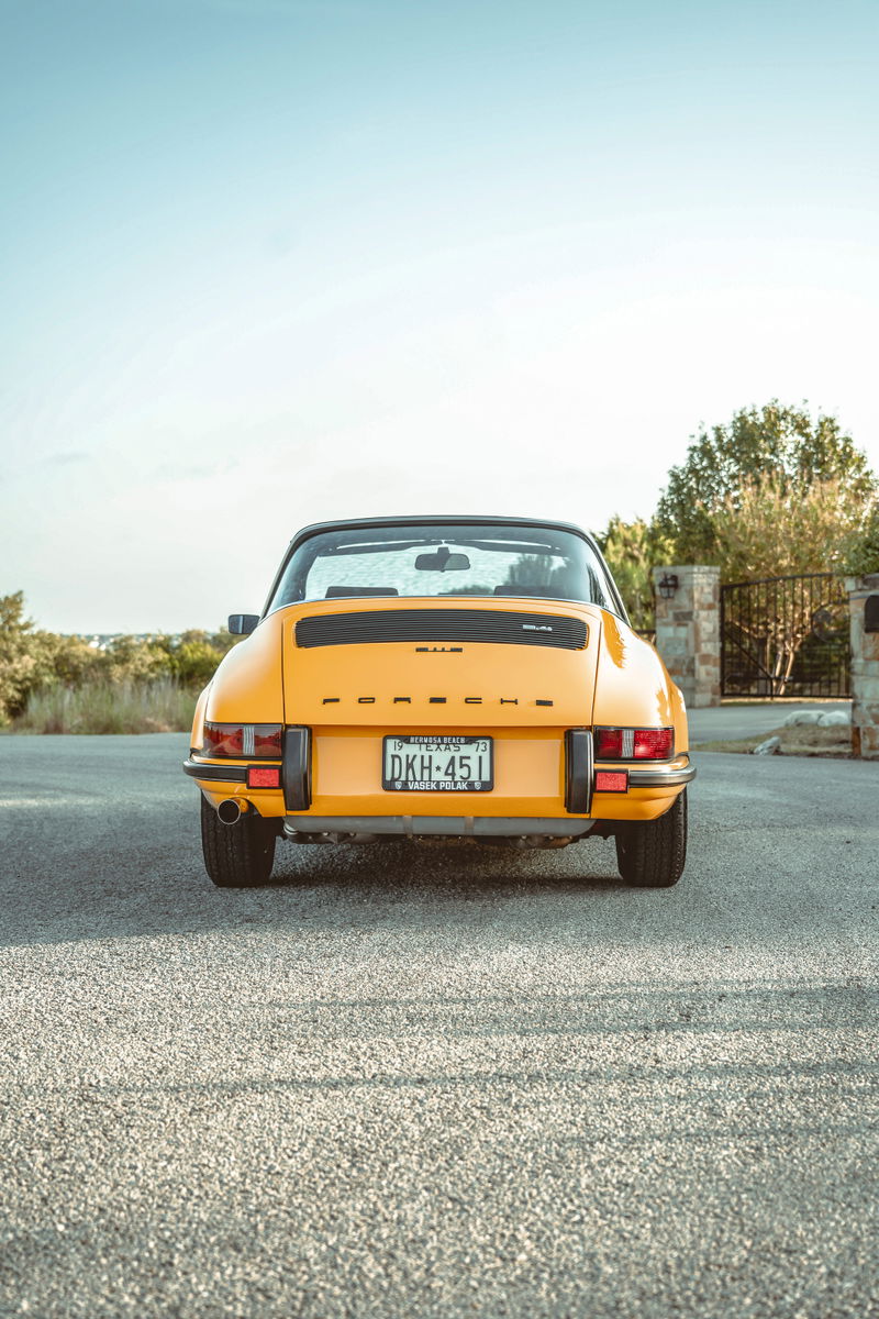 Rear view of a vibrant Signal Yellow 1973 Porsche 911S Targa. Features classic black bumperettes, single exhaust, and 'PORSCHE' script.