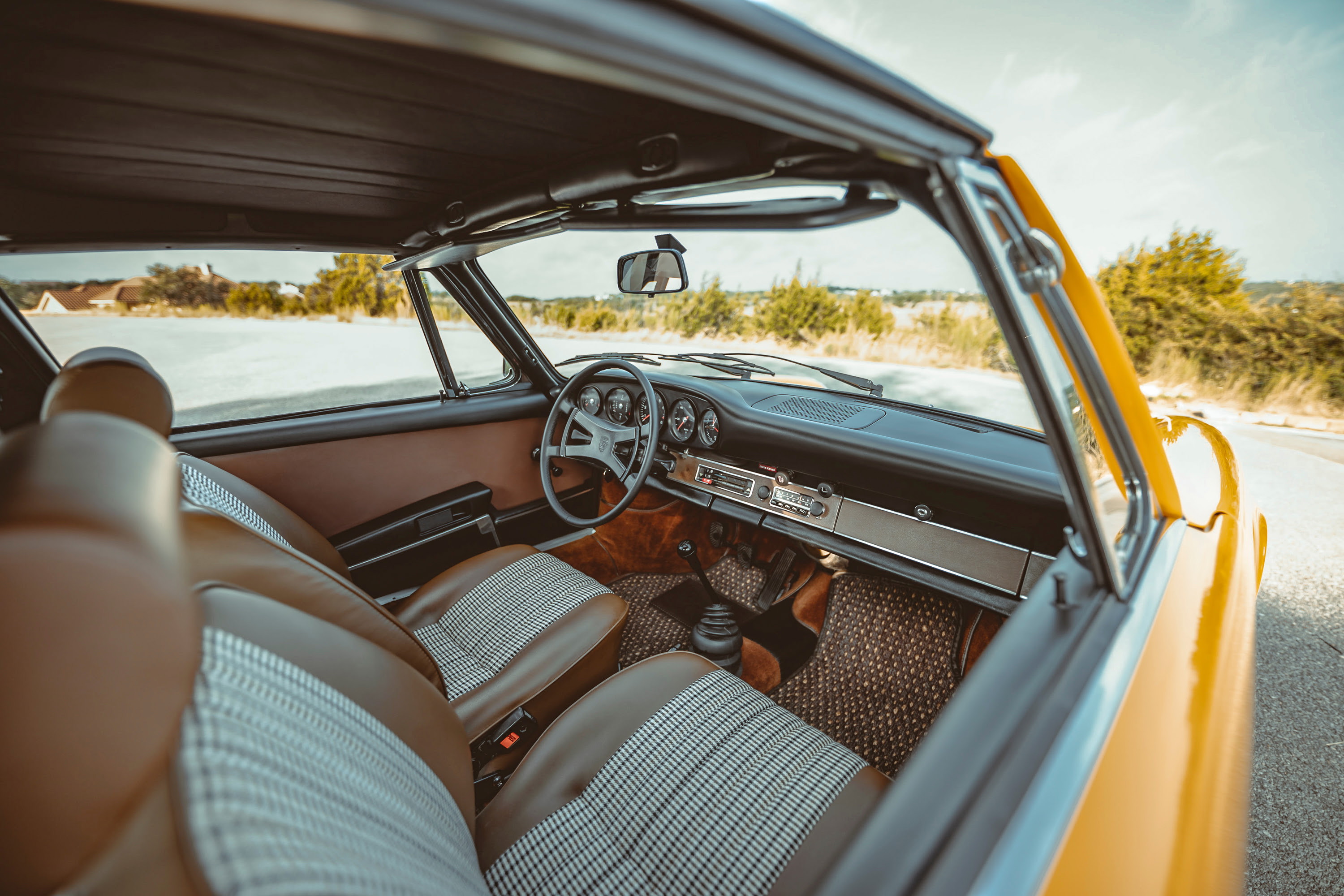 Interior of a 1973 Signal Yellow Porsche 911S Targa. Brown leatherette and pepita seats, classic dashboard, chrome trim.