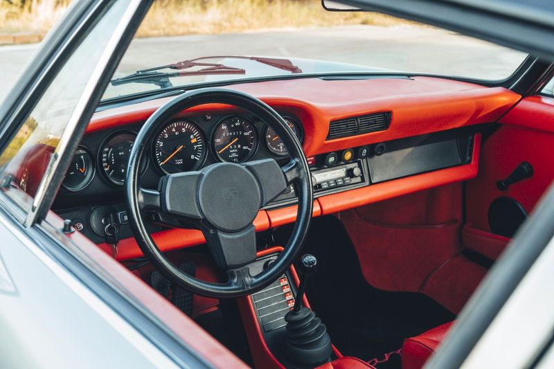 1977 Porsche 911S interior with bold red trim, classic five-dial gauge cluster, black steering wheel, and vintage stereo.