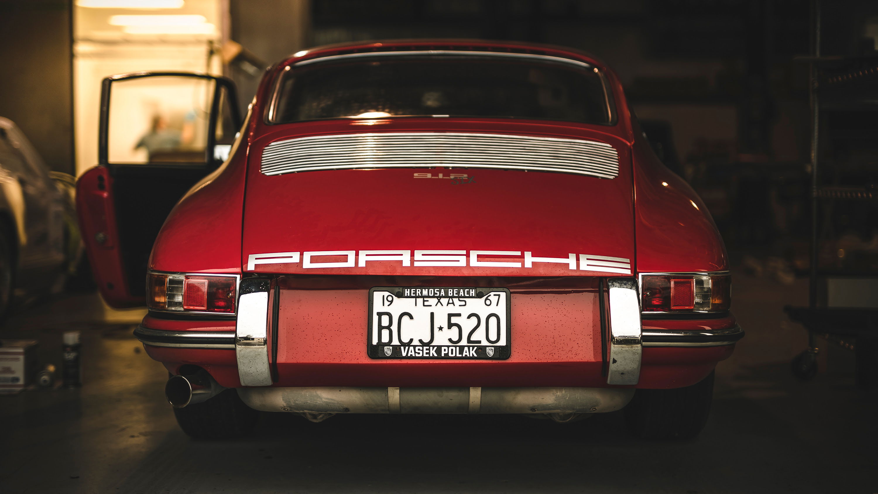 Rear view of a classic red 1967 Porsche 911 in a garage, featuring its iconic engine lid grille and chrome bumper.