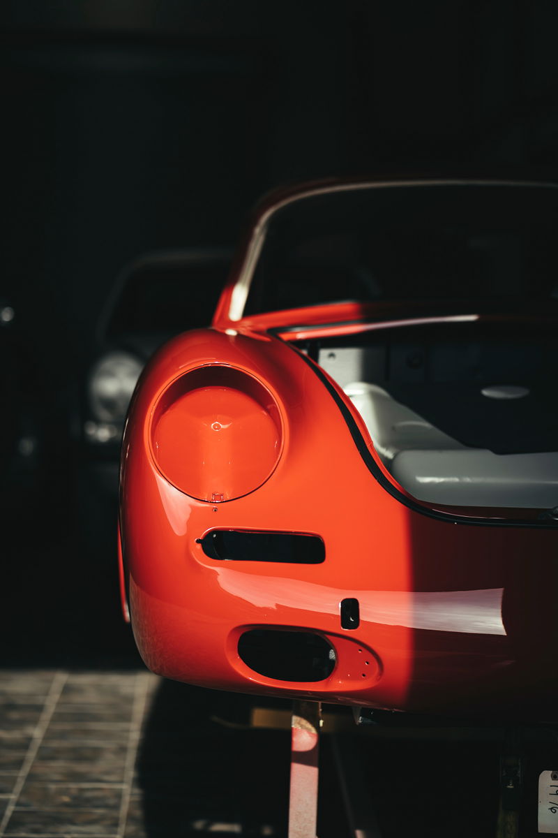 Close-up of a brilliant red Porsche 356 front fender & headlight recess during restoration, highlighting glossy paint & trim openings.