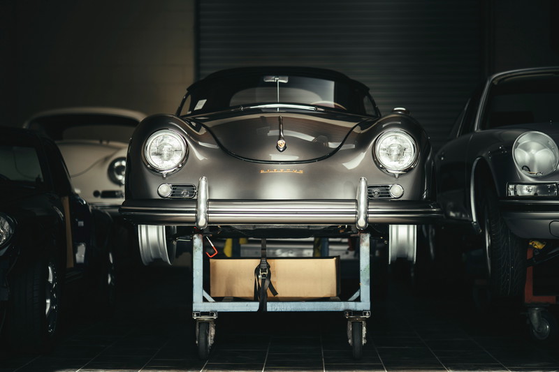 Gunmetal grey Porsche 356 coupe on a workshop dolly, featuring elegant chrome bumperettes and classic round headlights.