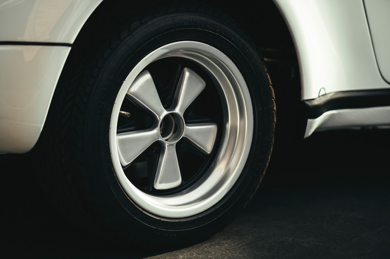 White classic air-cooled Porsche 911 with polished Fuchs 5-spoke alloy wheels, black centers, and black rocker trim.