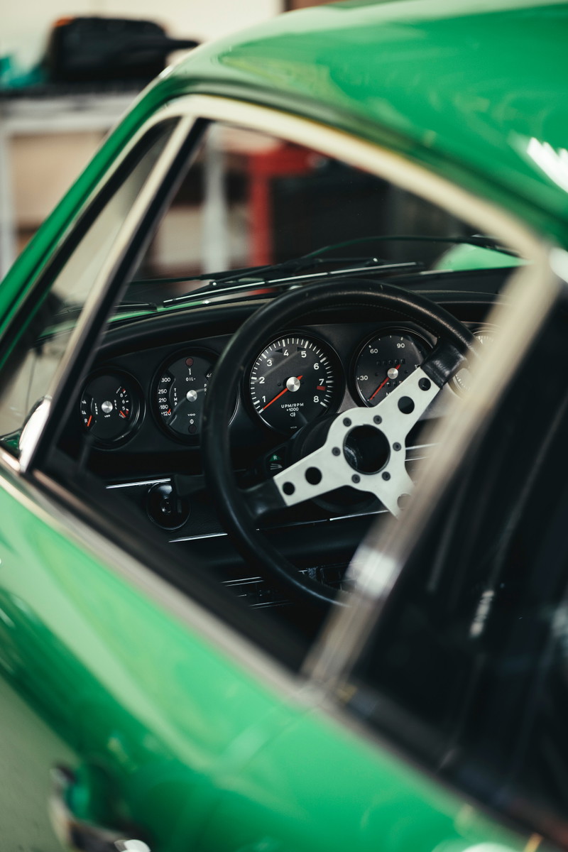 Green classic Porsche 911 interior at Lit Show LA, featuring its black 5-dial gauges and drilled racing steering wheel.