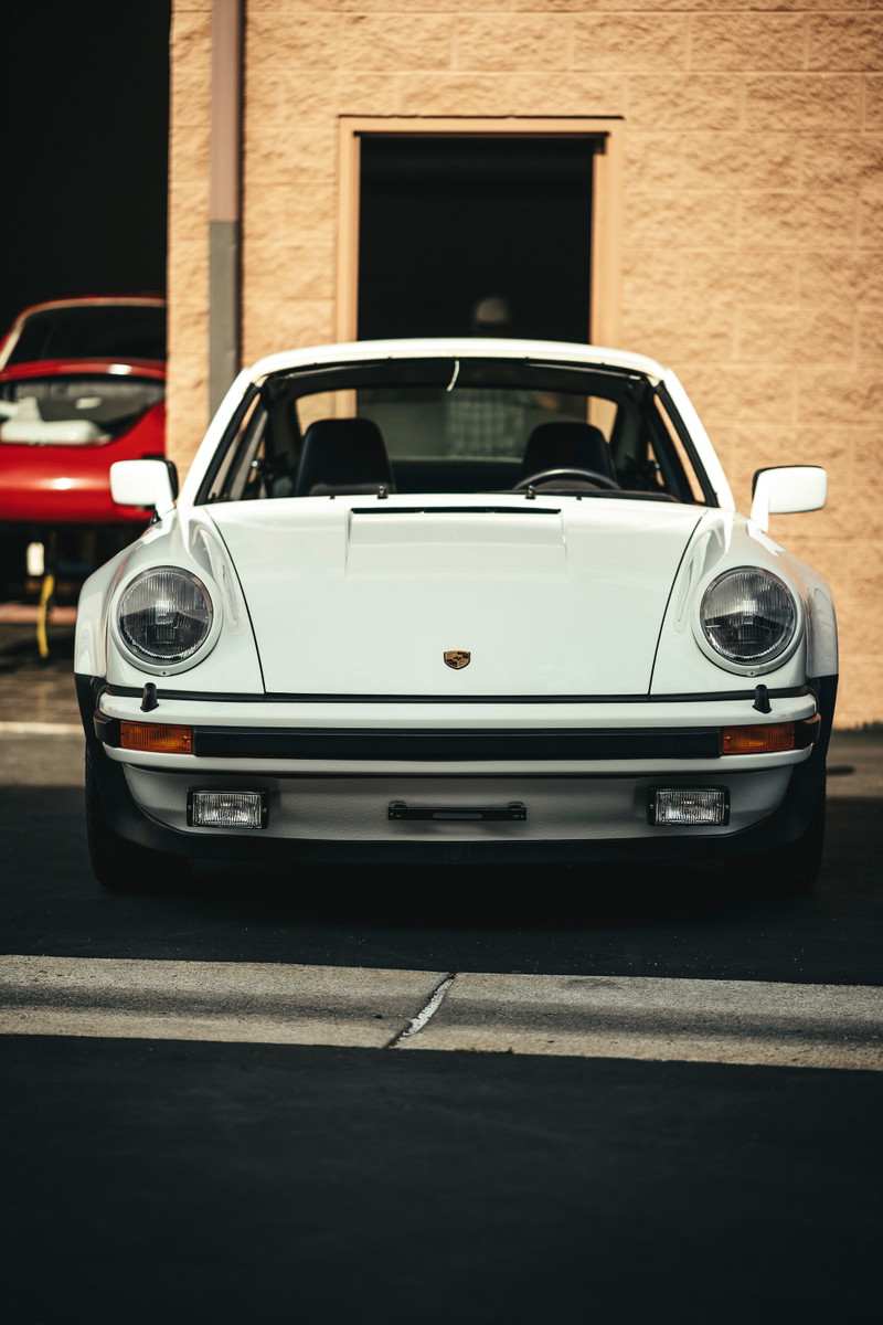 Frontal view of a pristine white classic Porsche 911 G-series with iconic round headlamps and black impact bumpers.