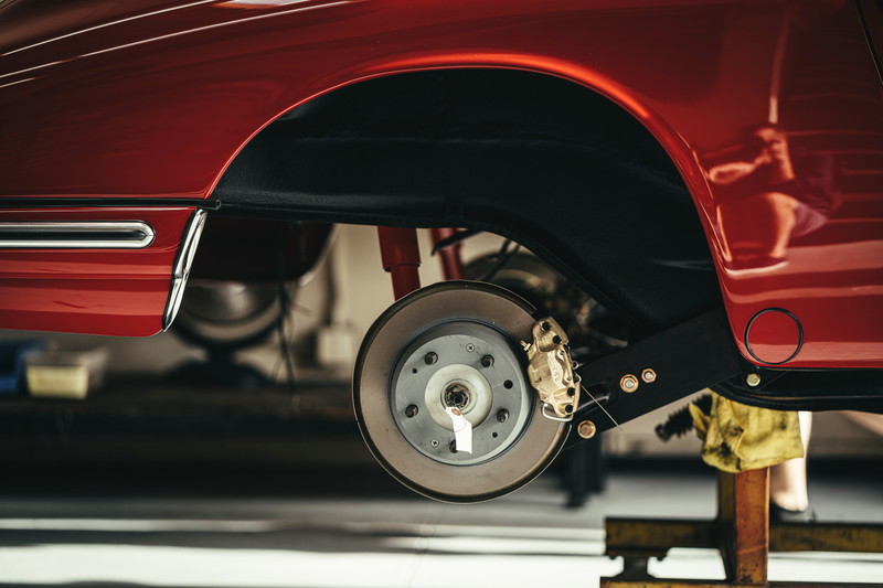 Red classic air-cooled Porsche 911 with exposed brake rotor, gold caliper, and suspension in the rear wheel arch.
